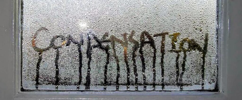 A window covered in a high level of moisture, with the word "CONDENSATION" written through the fog and water droplets streaming down the glass.